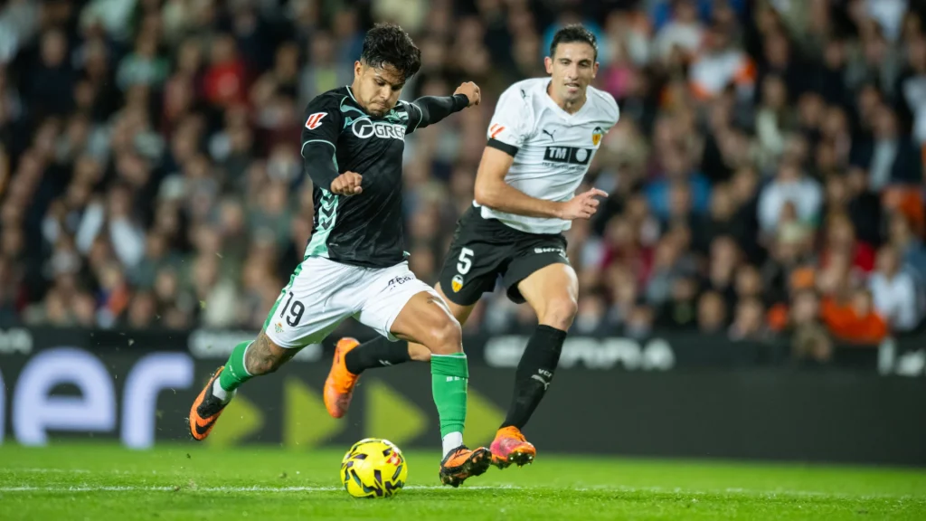 El delantero bético Cucho Hernández se dispone a ejecutar un disparo a portería ante la mirada del defensa valencianista César Tárrega en el Valencia - Betis previo al parón de selecciones.