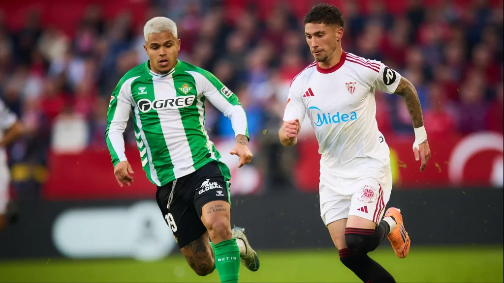 Carmona (Sevilla) y Cucho Hernández (Real Betis) persiguen un balón en el lateral del campo durante el derbi sevillano.