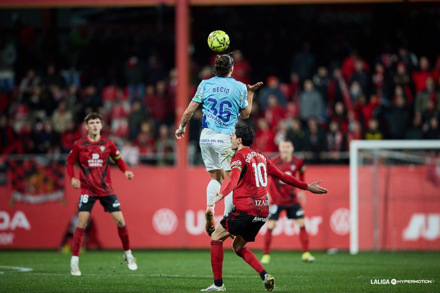 Recio (Málaga) peina un balón en medio campo ante un Carlos Fernández (Mirandés)  que protesta una acción durante el partido de Liga Hypermotion que cerraba la jornada.